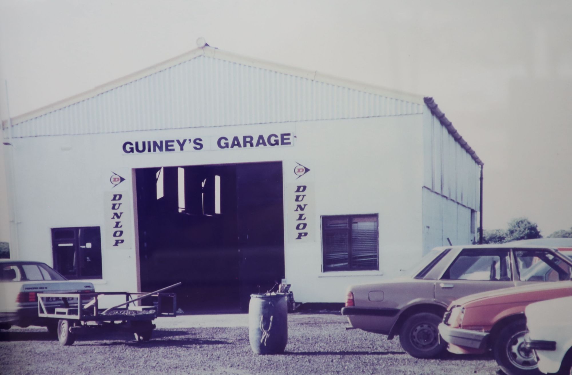 Three assorted near contemporary photographs, Woodland in winter, Coastal scene and Guineys Garage, largest 50 x 76cm